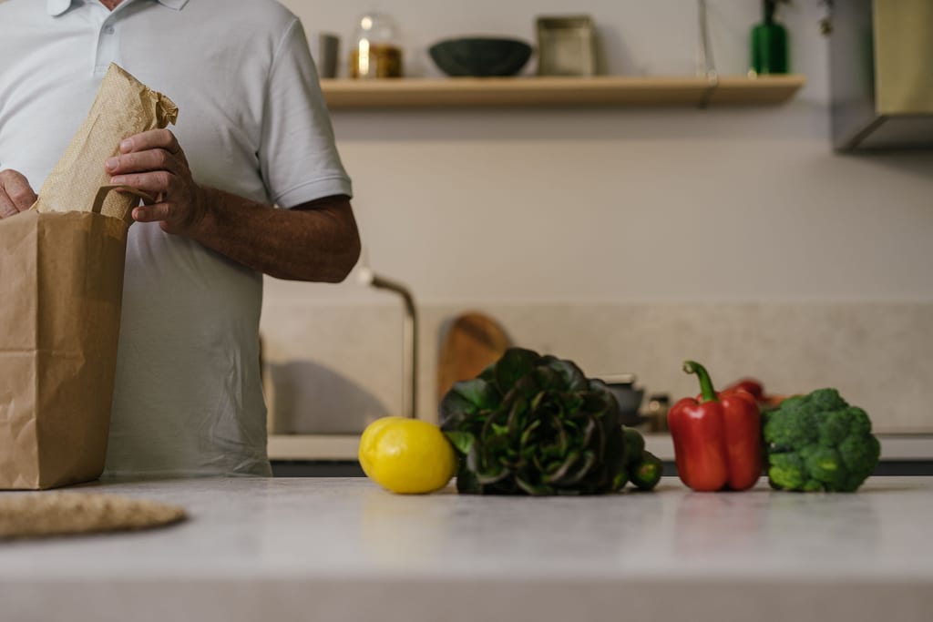 Unpacking a paper grocery bag onto a kitchen bench: lemon, lettuce, capsicum and broccoli